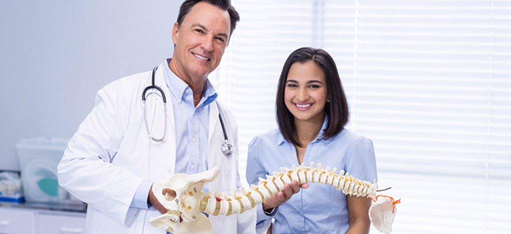 Hispanic-chiropractor-in-San-Antonio-holding-a-model-of-the-spine-and-smiling